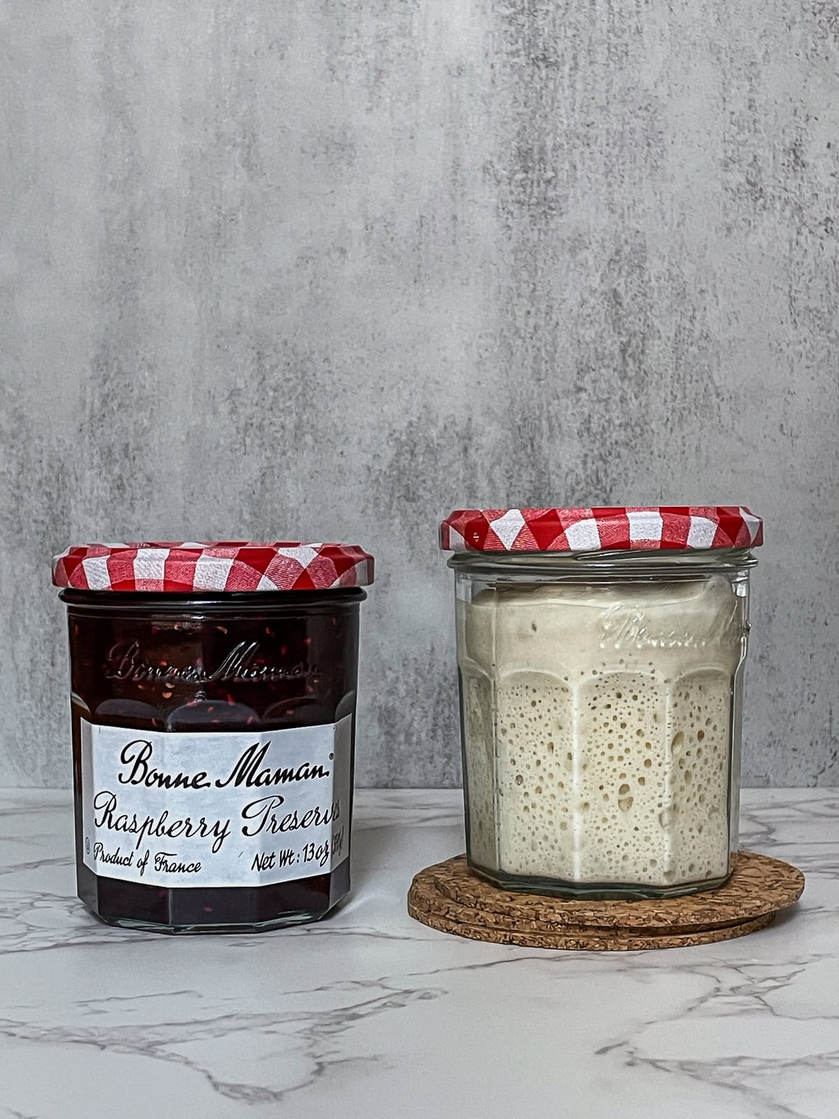 Two jars: one is a sourdough starter jar with a starter, and the other contains preserves.
