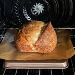 Sourdough bread on a baking sheet lined with parchment in the oven.