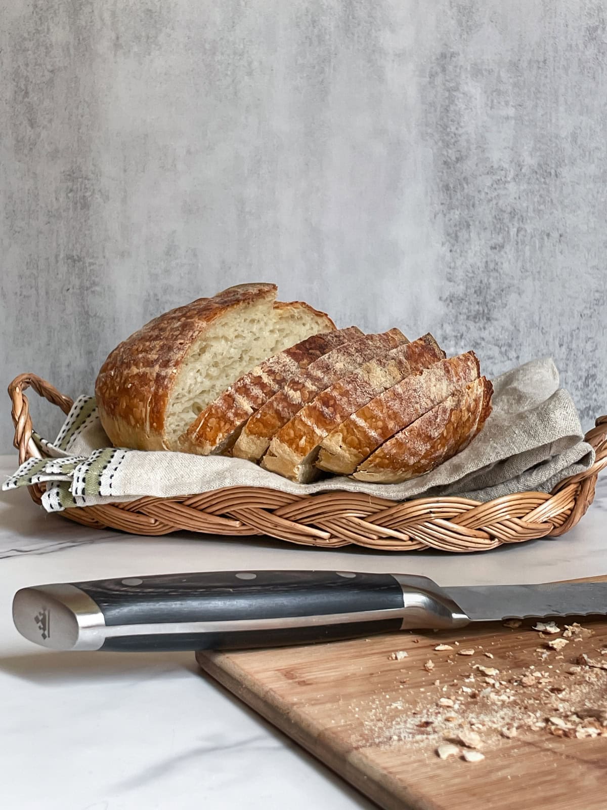 Sliced sourdough loaf in a bread basket, with a bread knife on a cutting board.
