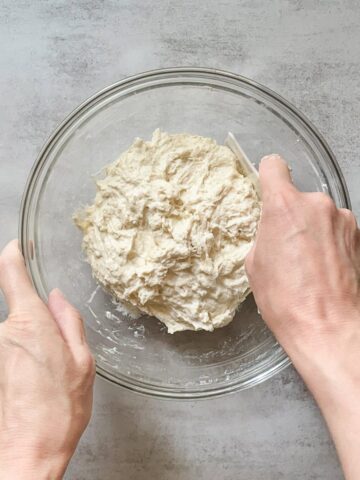 Sourdough mixed with a bowl scraper for autolyse in a glass mixing bowl.