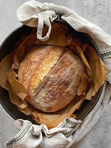 A Dutch oven with sourdough bread wrapped in a kitchen towel.
