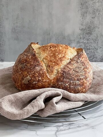 Sourdough bread with a single slash on a wire rack lined with a tea towel.