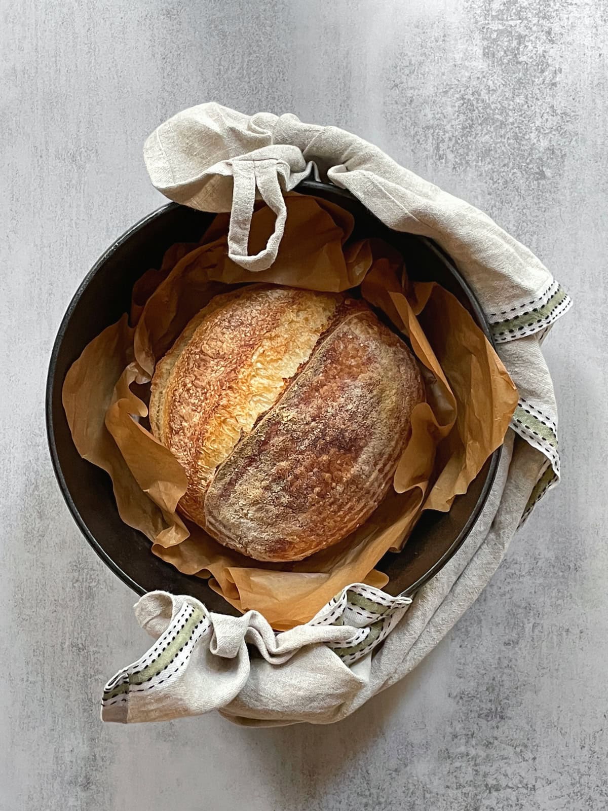 A Dutch oven with sourdough loaf wrapped in a kitchen towel.
