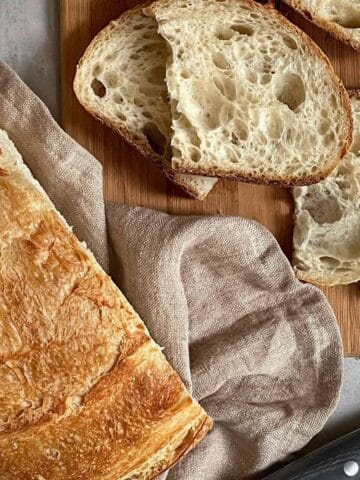 Sliced sourdough boule on a tea towel and cutting board.