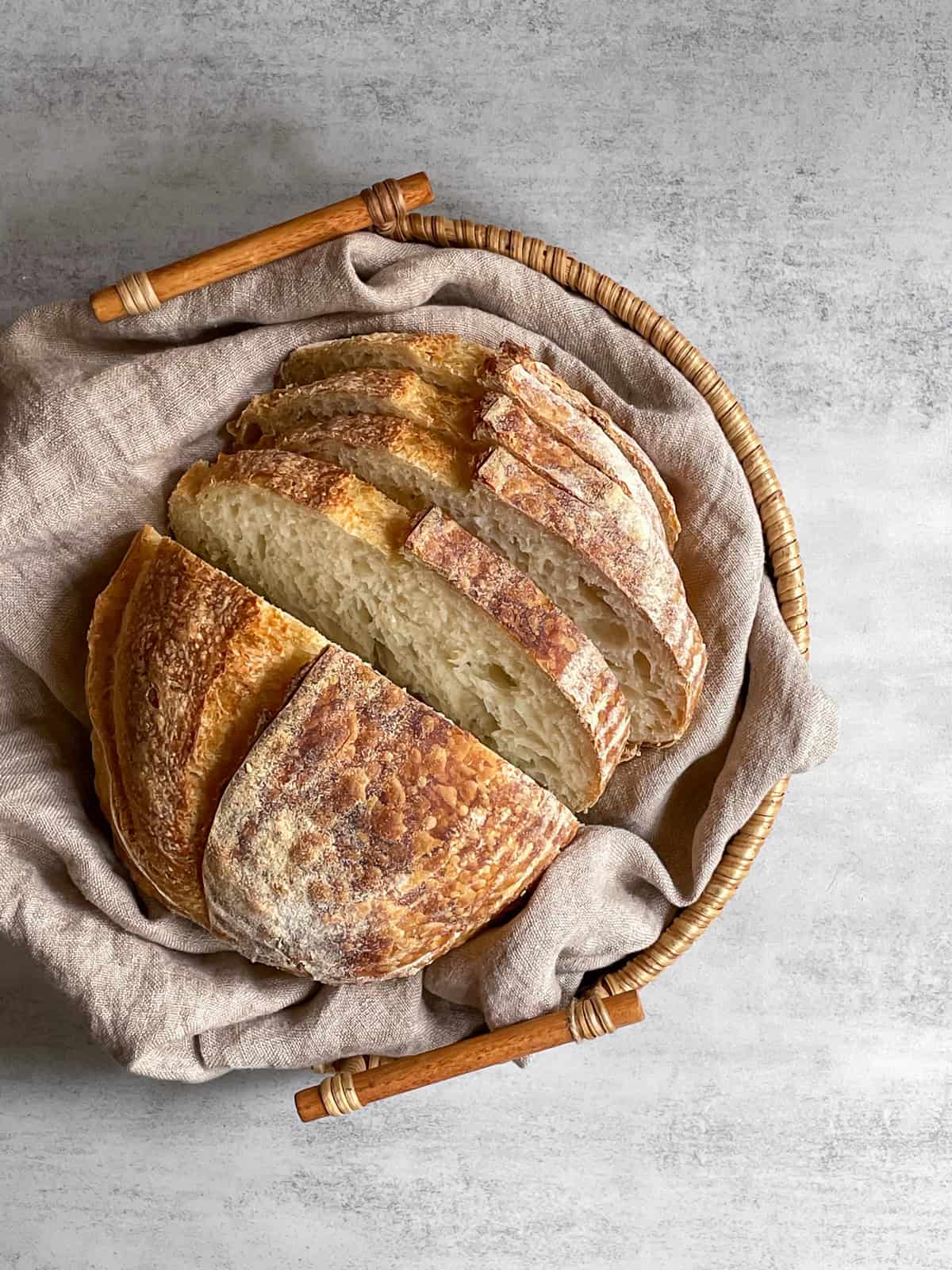 Sliced sourdough loaf placed in a woven basket lined with a kitchen towel.