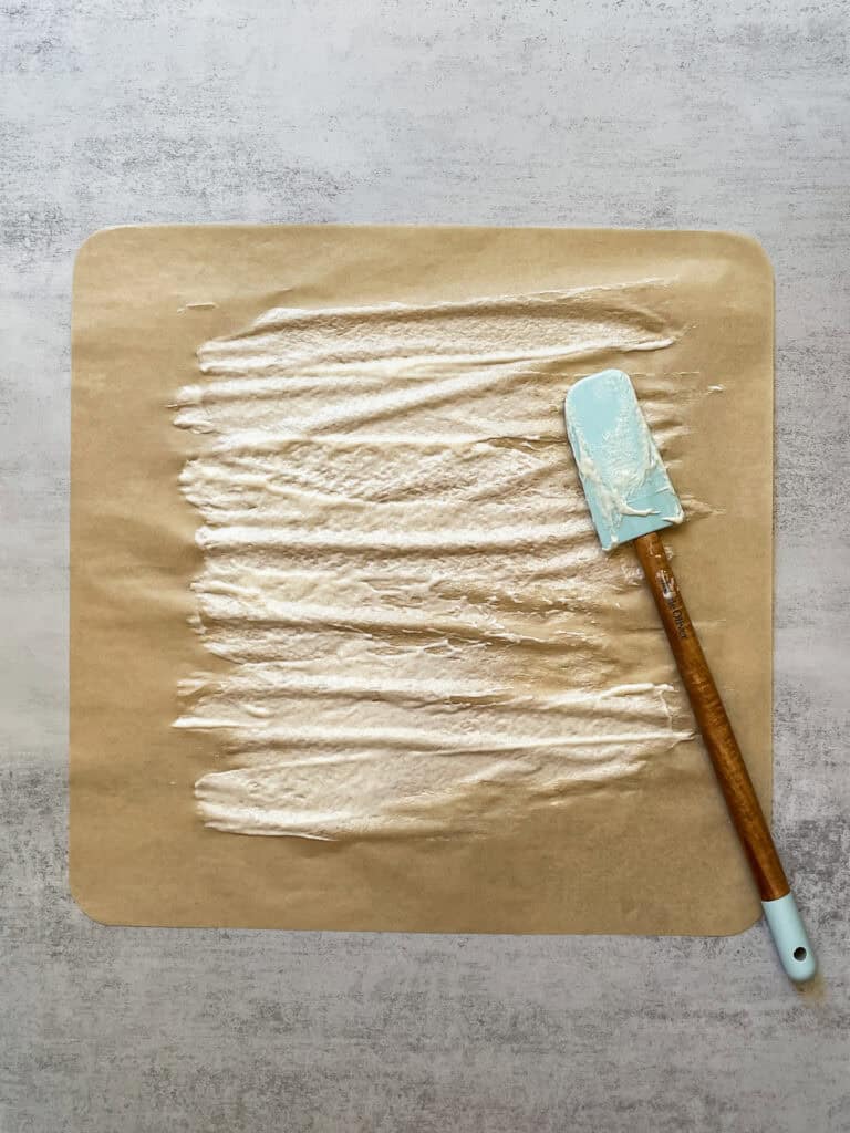 Drying sourdough starter on parchment paper with a spatula nearby.