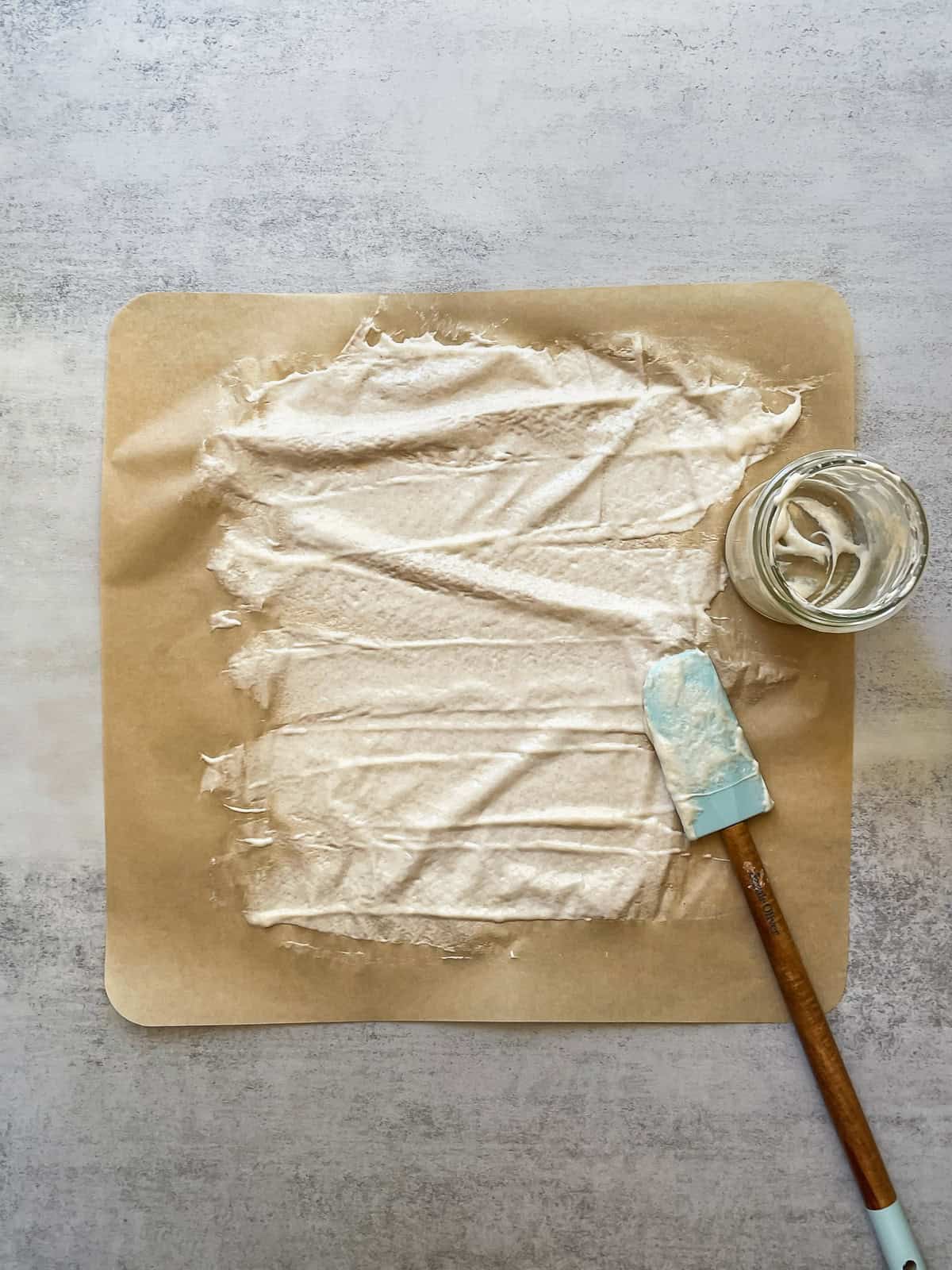 Sourdough starter spread on parchment paper with a spatula and a jar nearby.