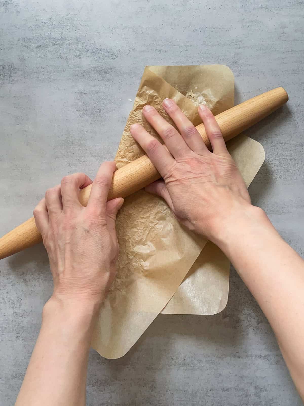 Grinding dried sourdough starter with a rolling pin and hands.