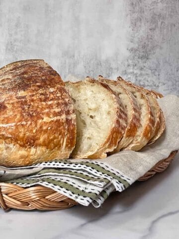 Tangy sliced sourdough bread in a towel-lined basket, made using tips to boost the sour flavor.