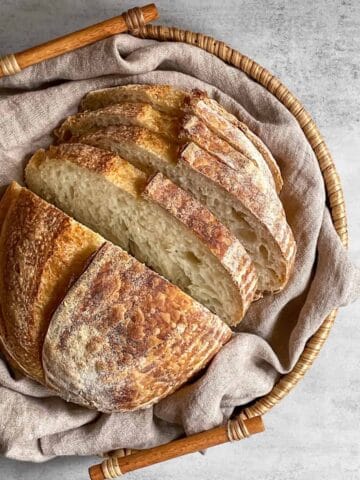 Sliced sourdough bread arranged in a woven basket lined with a kitchen towel.