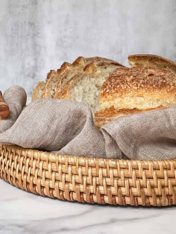 Tangy, freshly sliced sourdough bread in a basket with a tea towel, showing its crisp crust and soft crumb.