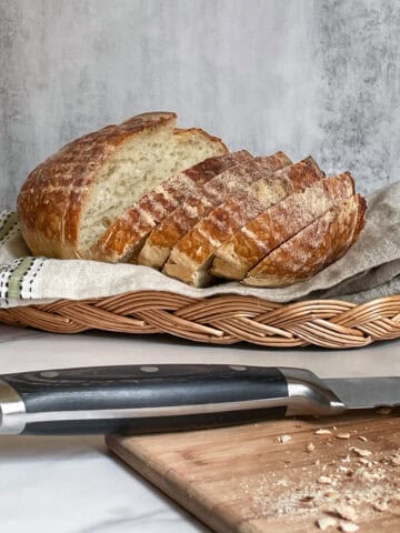Sliced sourdough bread in a bread basket, with a bread knife on a cutting board.