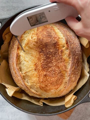 Sourdough bread in a Dutch oven, with a probe thermometer checking the internal temperature of baked bread.