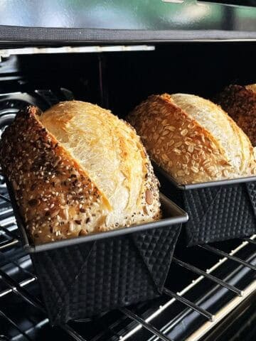Three loaf pans with sourdough sandwich bread in the oven.