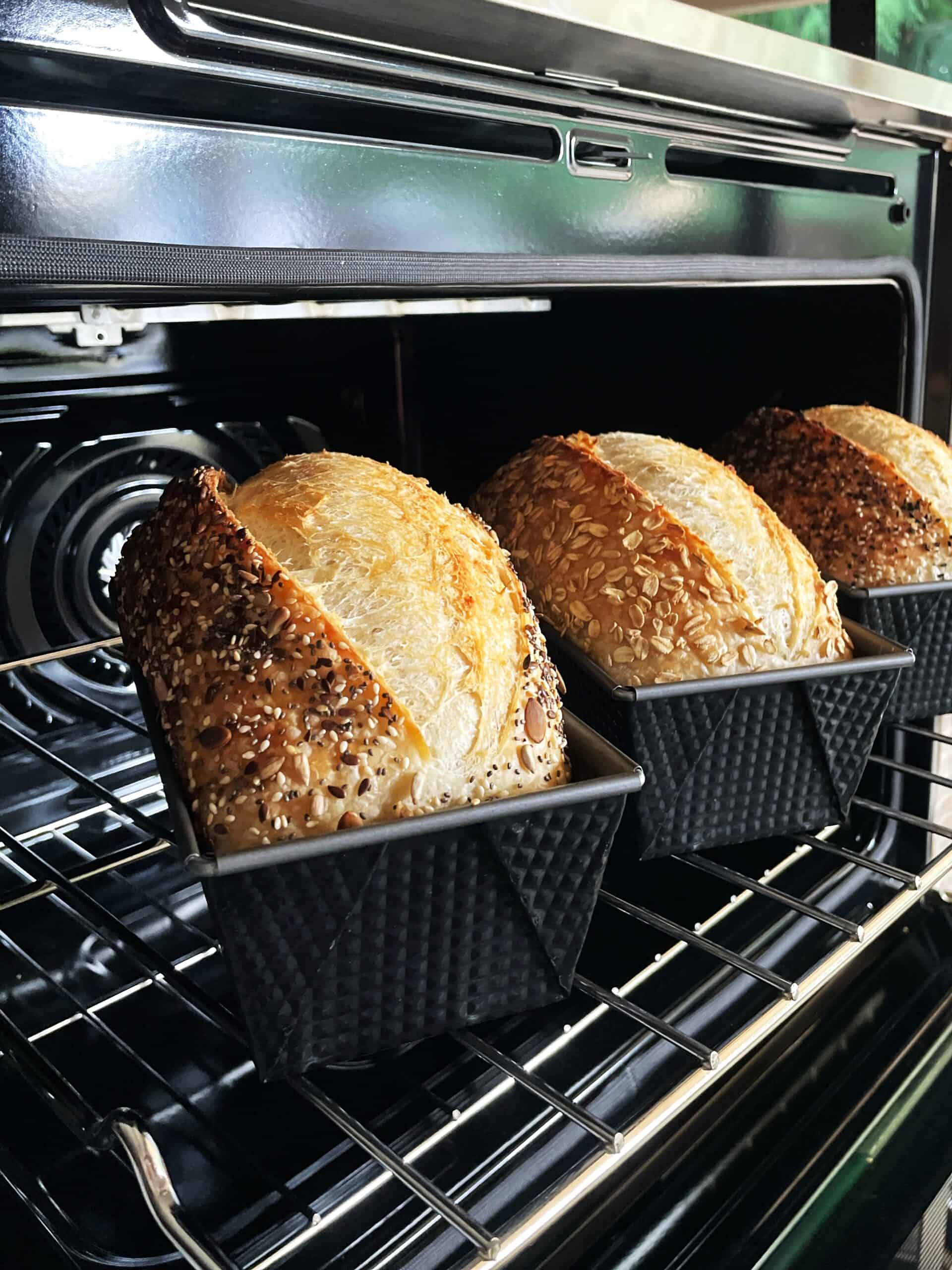 Three loaf pans with sourdough bread in the oven.