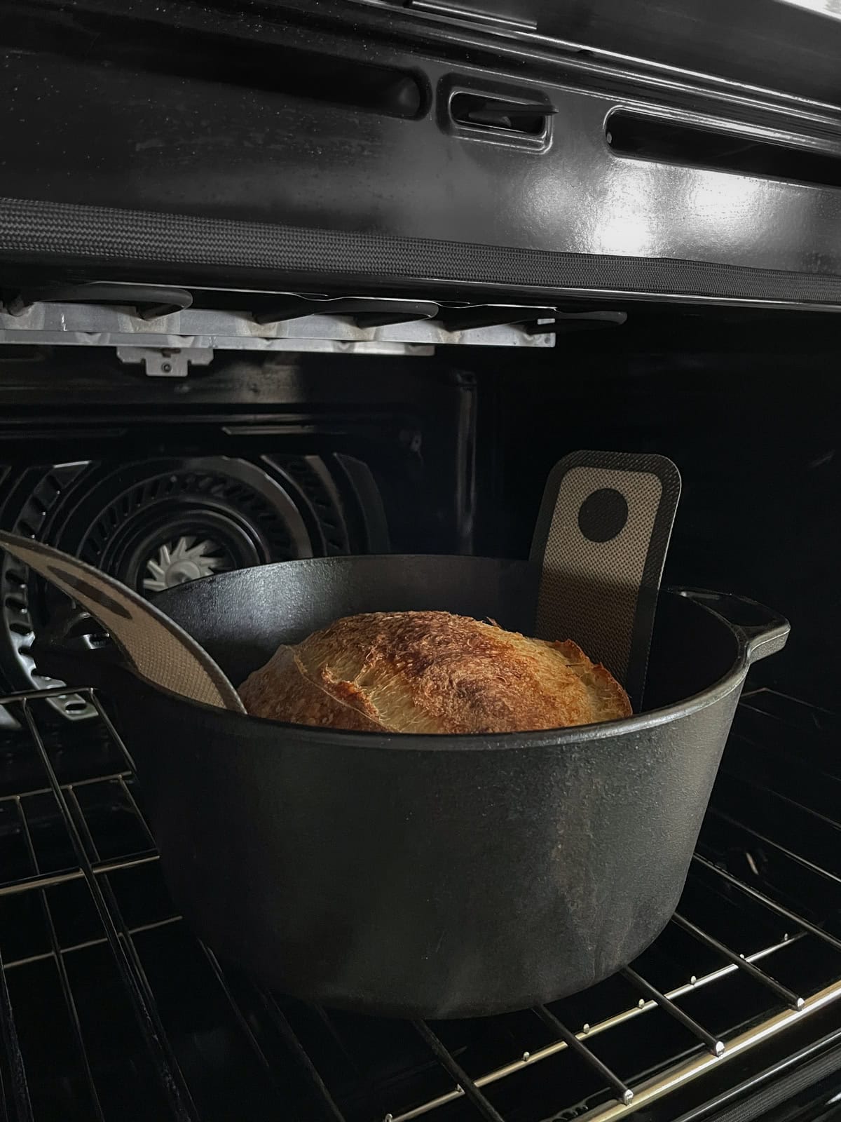 Sourdough bread in a Dutch oven, lined with a silicone bread sling.