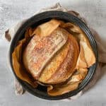Sourdough bread in a granite ware roaster lined with parchment paper.