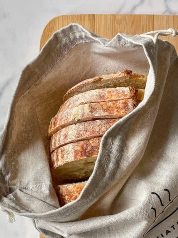 True sourdough bread in a bread bag resting on a cutting board.