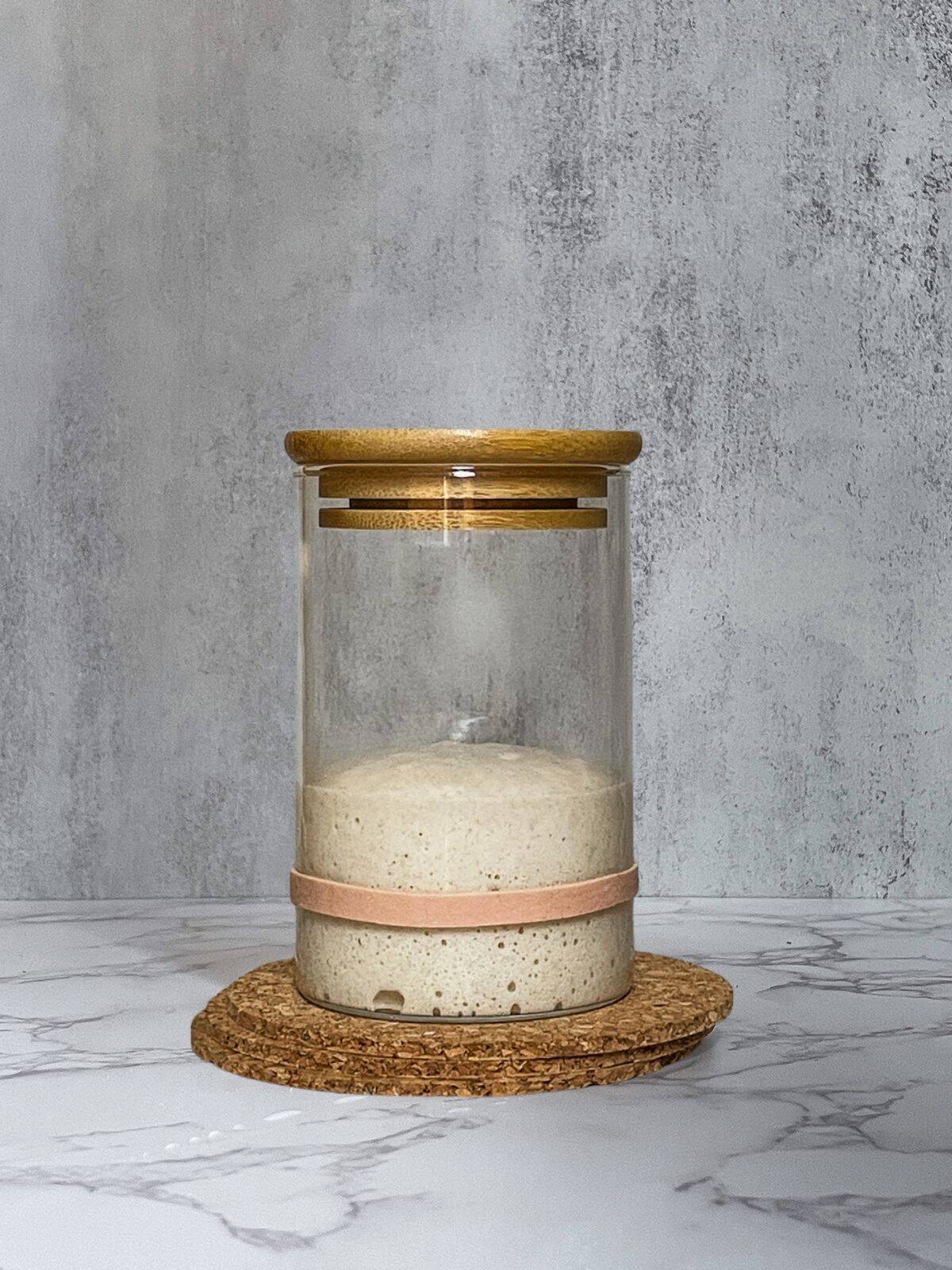 Sourdough starter with domed top in a glass jar.