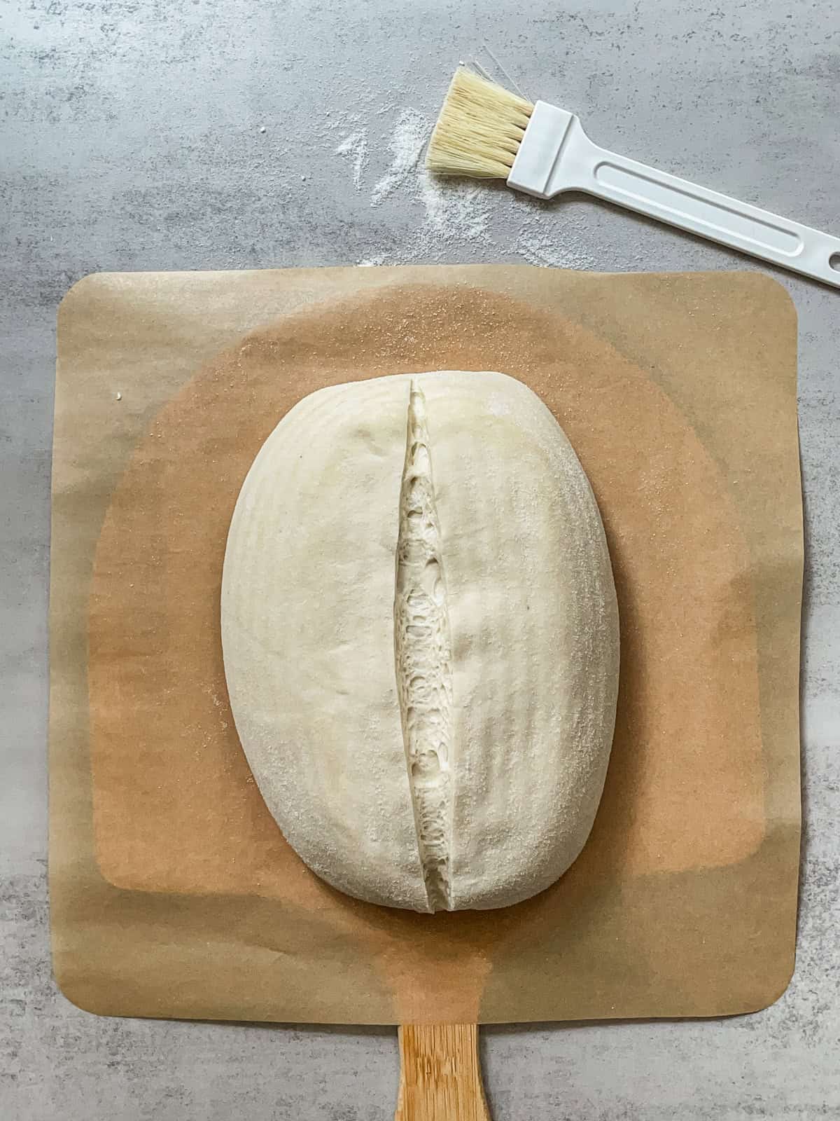 Batard with a single slash on a parchment-lined pizza peel.