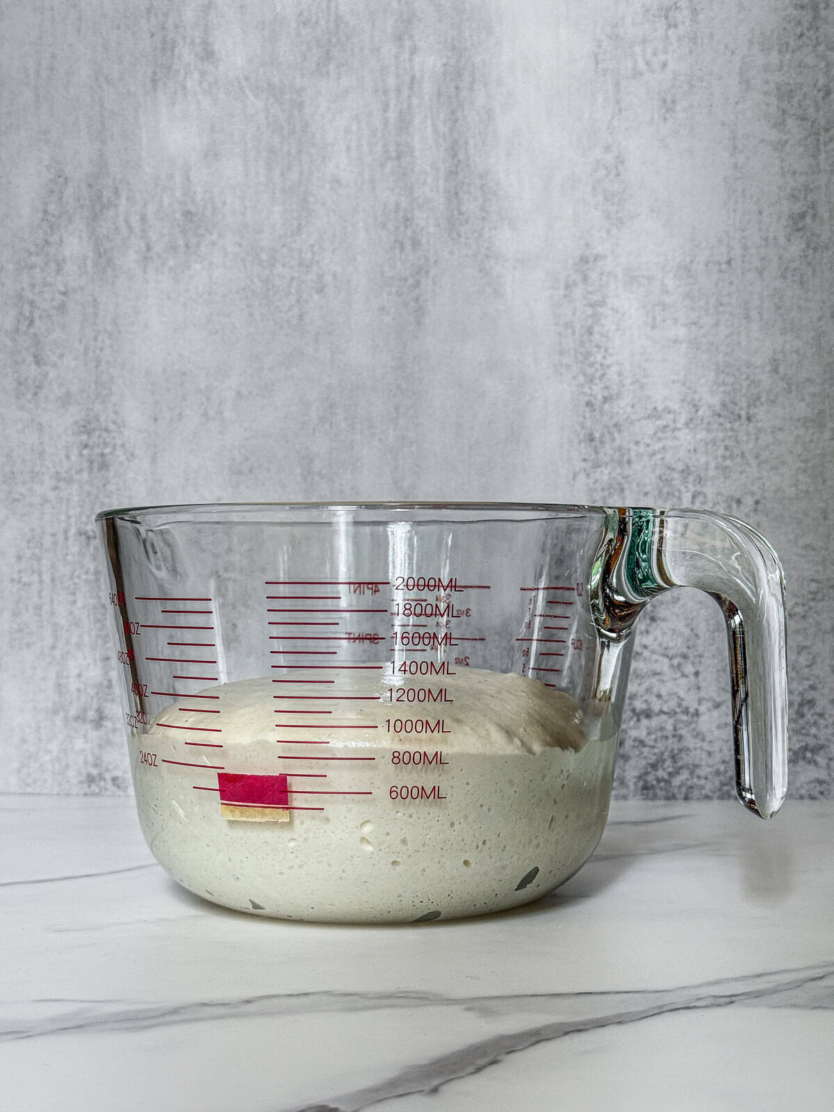 Dough in a measuring cup at mid-bulk fermentation, front view.