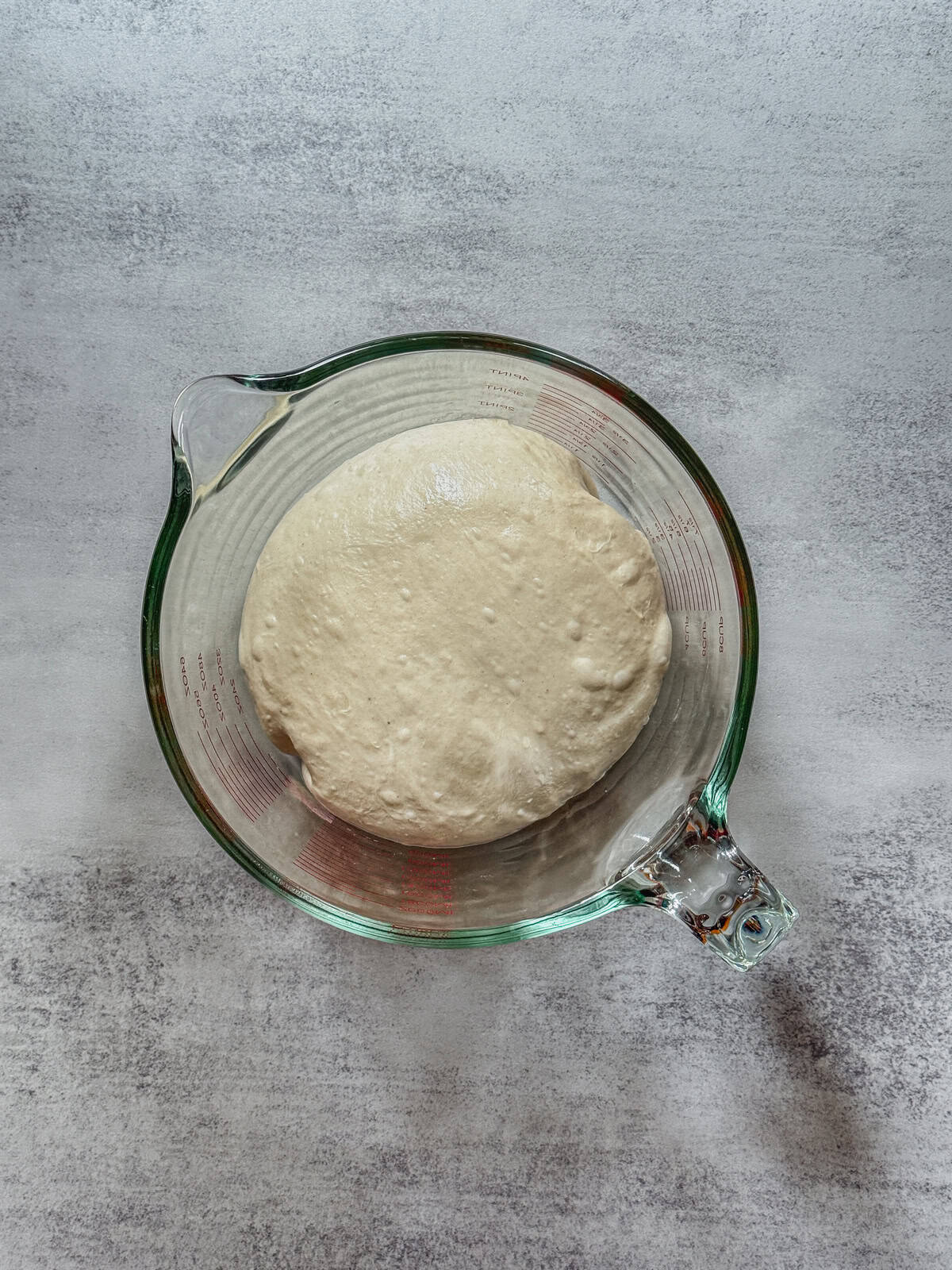 Dough in a measuring cup at mid-bulk fermentation, overhead view.