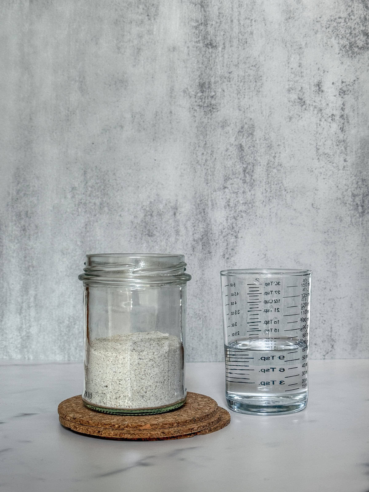 Jar with rye flour and a measuring glass of water beside it.