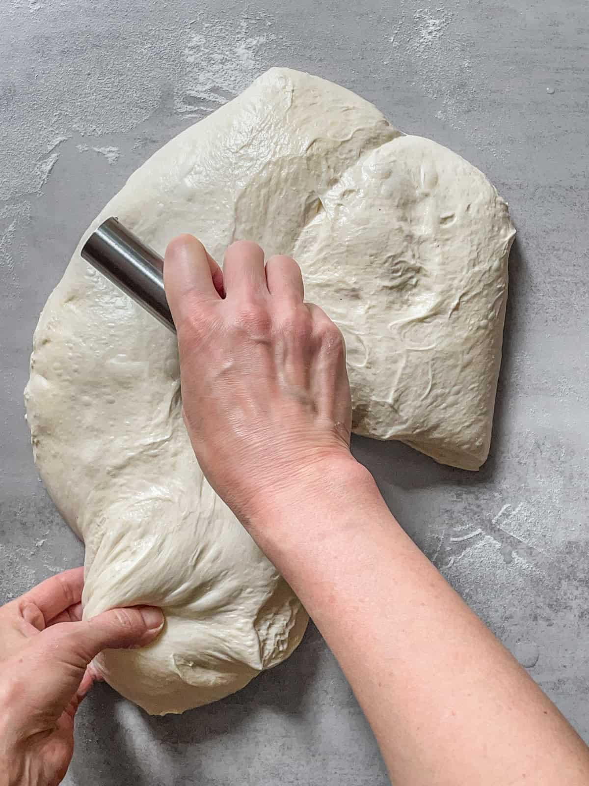 Bread dough with a bench scraper in hand being divided on a table.