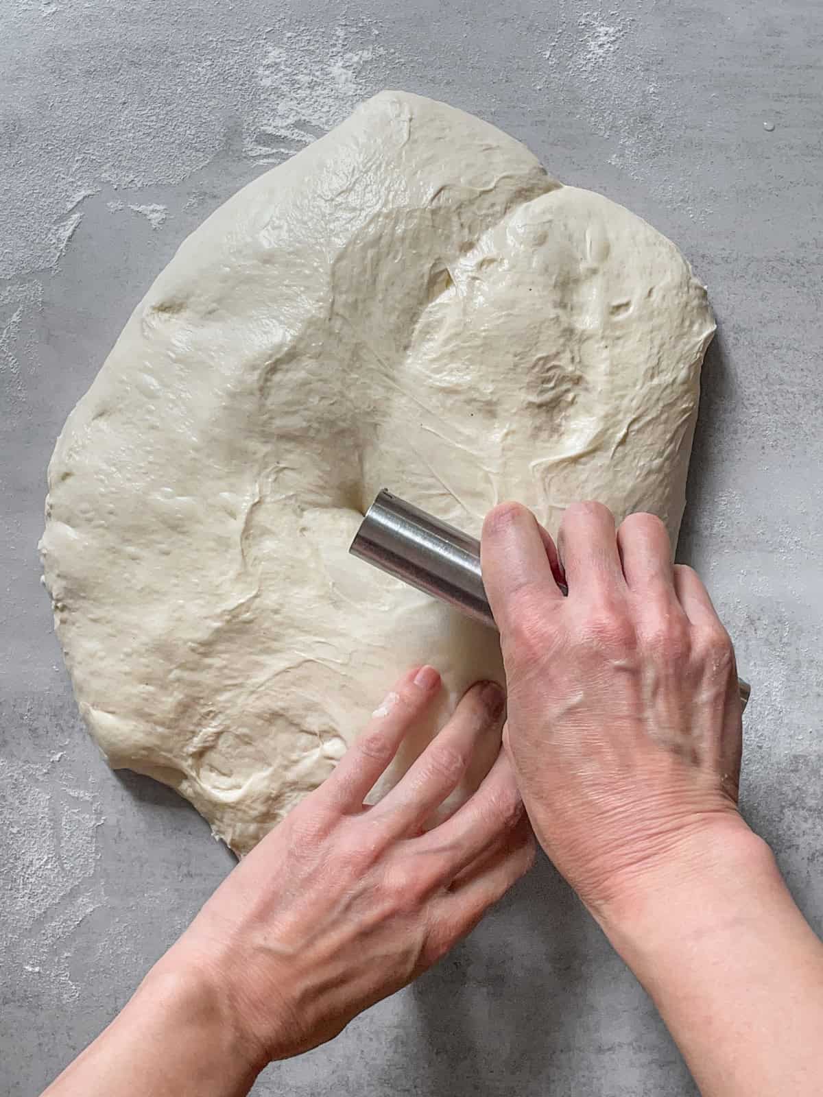 Sourdough with a bench scraper in hand being divided on a table.