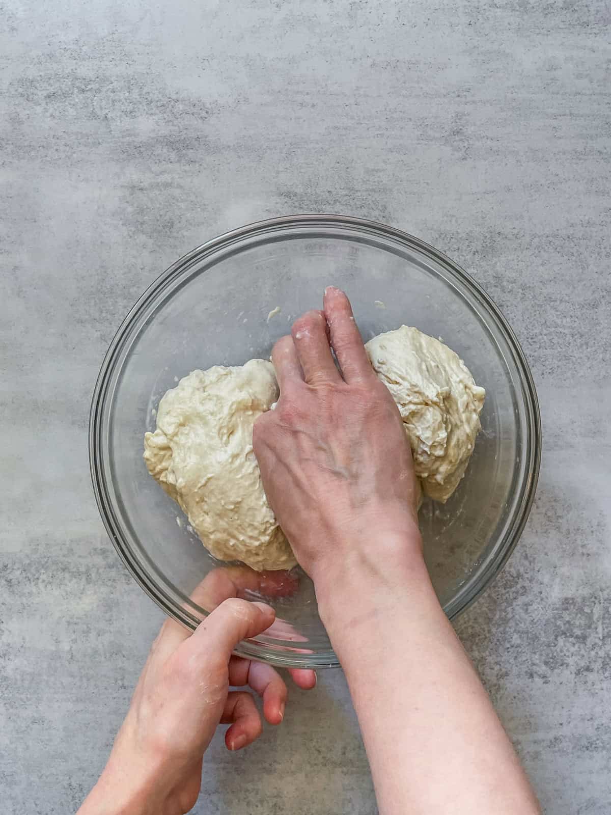 A hand pinching sourdough dough in a mixing bowl.