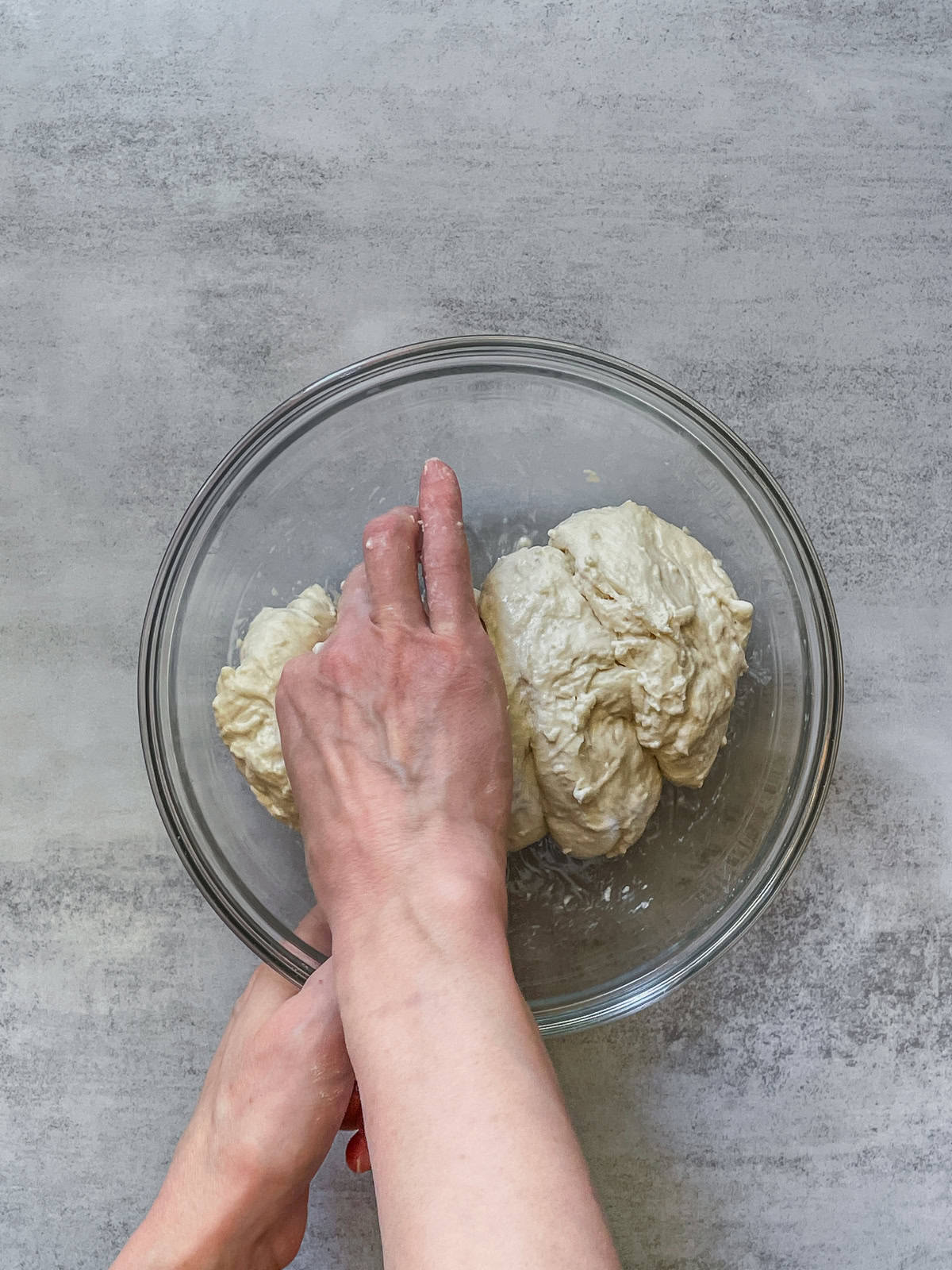A hand pinching bread dough in a mixing bowl.