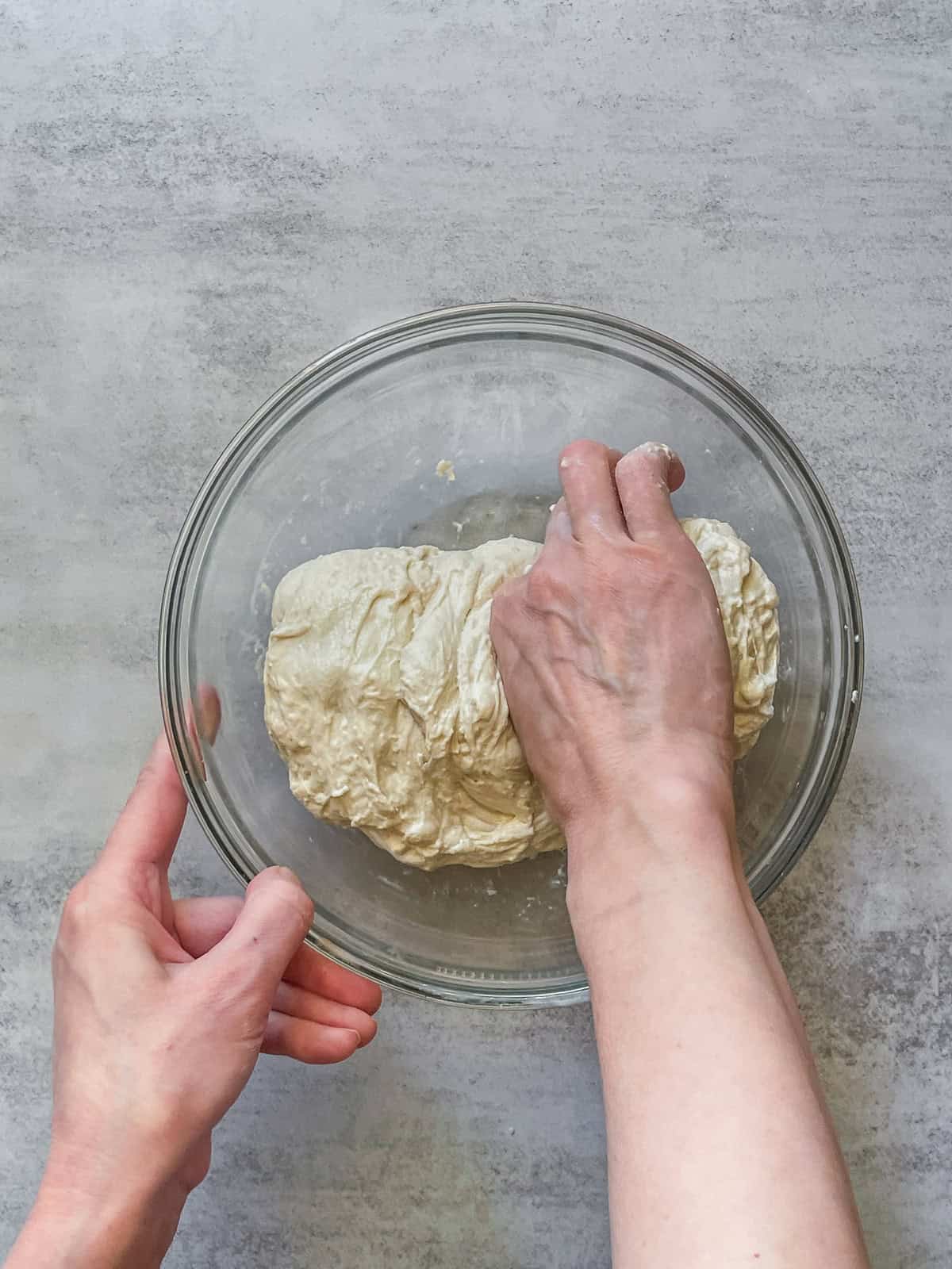 A hand pinching the dough in a mixing bowl.