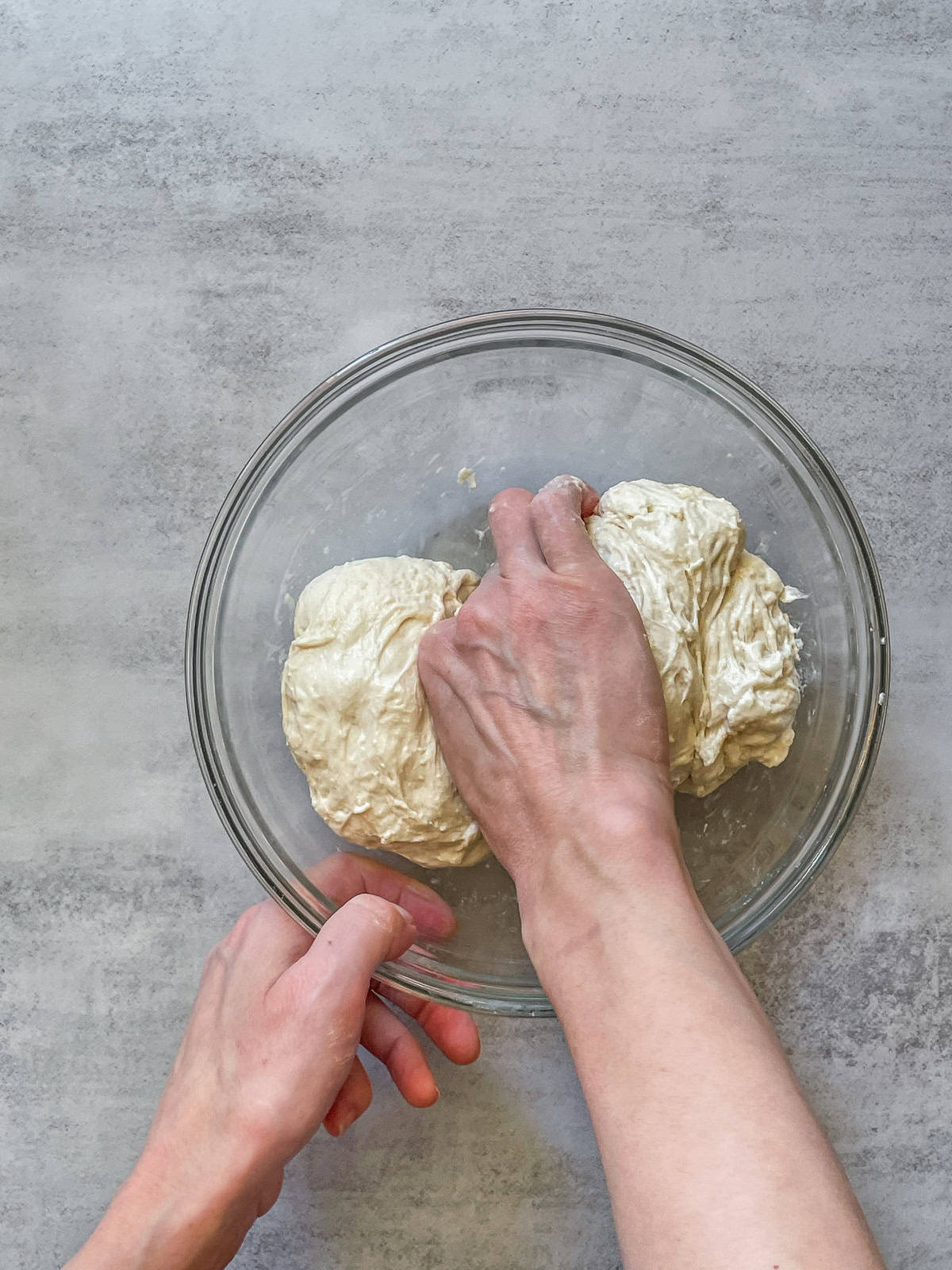 A hand pinching the dough in a glass mixing bowl.