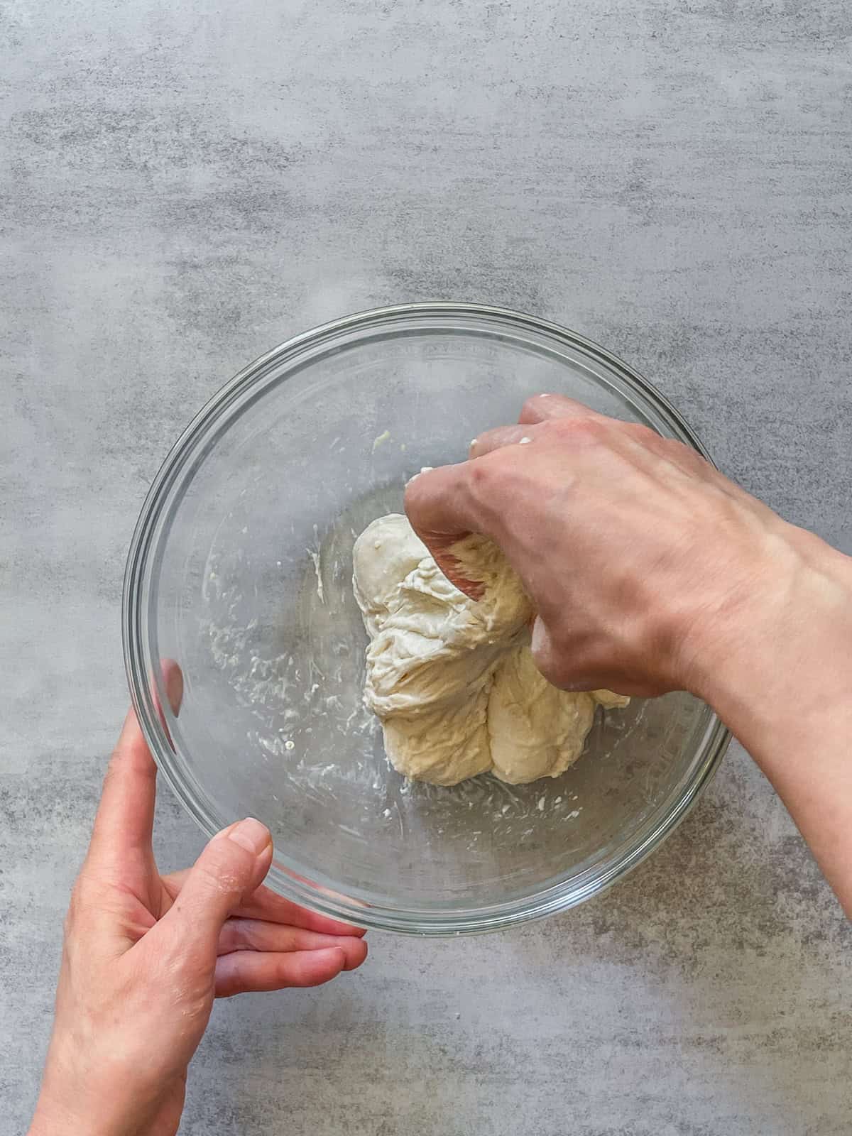 A hand folding the dough in a mixing bowl.