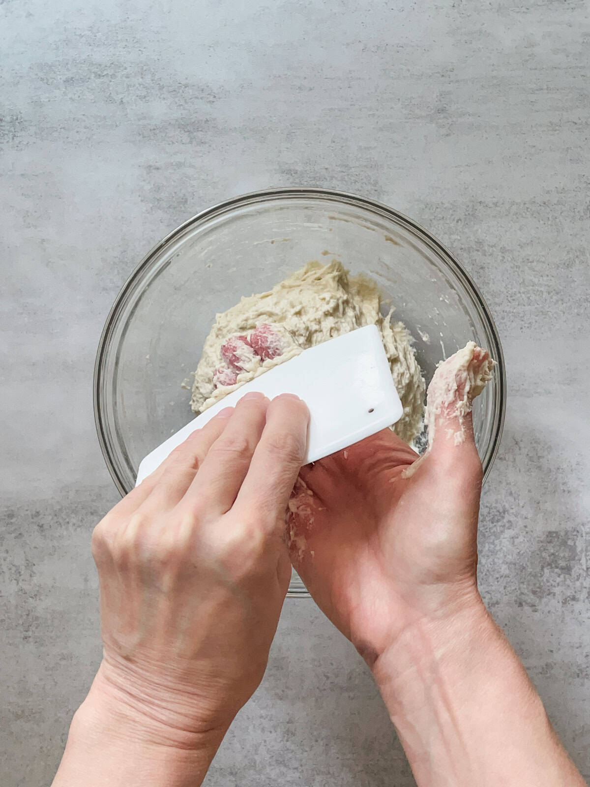 Hand using a plastic bowl scraper to clean dough off the other hand.
