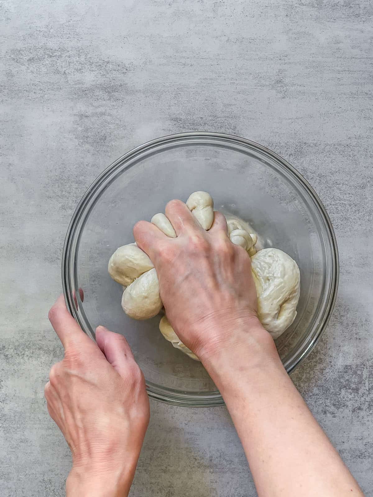 A hand squeezing sourdough dough in a mixing bowl.