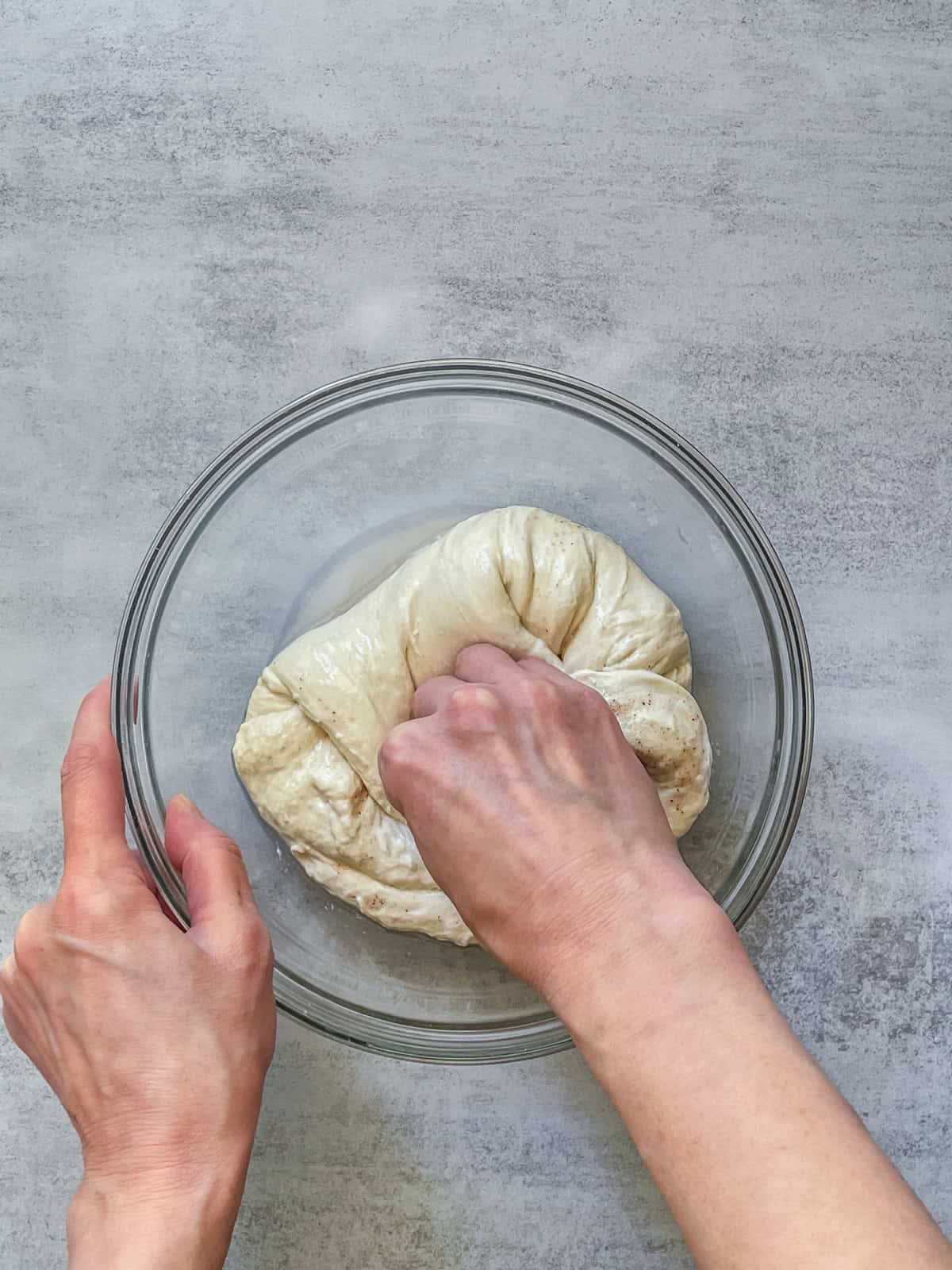 A hand folding sourdough dough toward the center in a bowl.