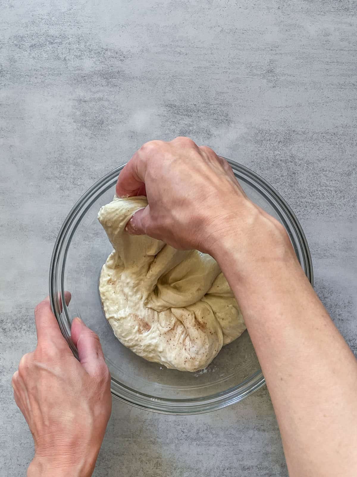 A hand grabbing and lifting sourdough dough in a bowl.