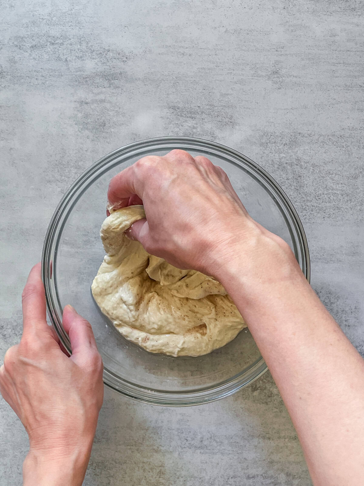 A hand lifting sourdough dough in a bowl.
