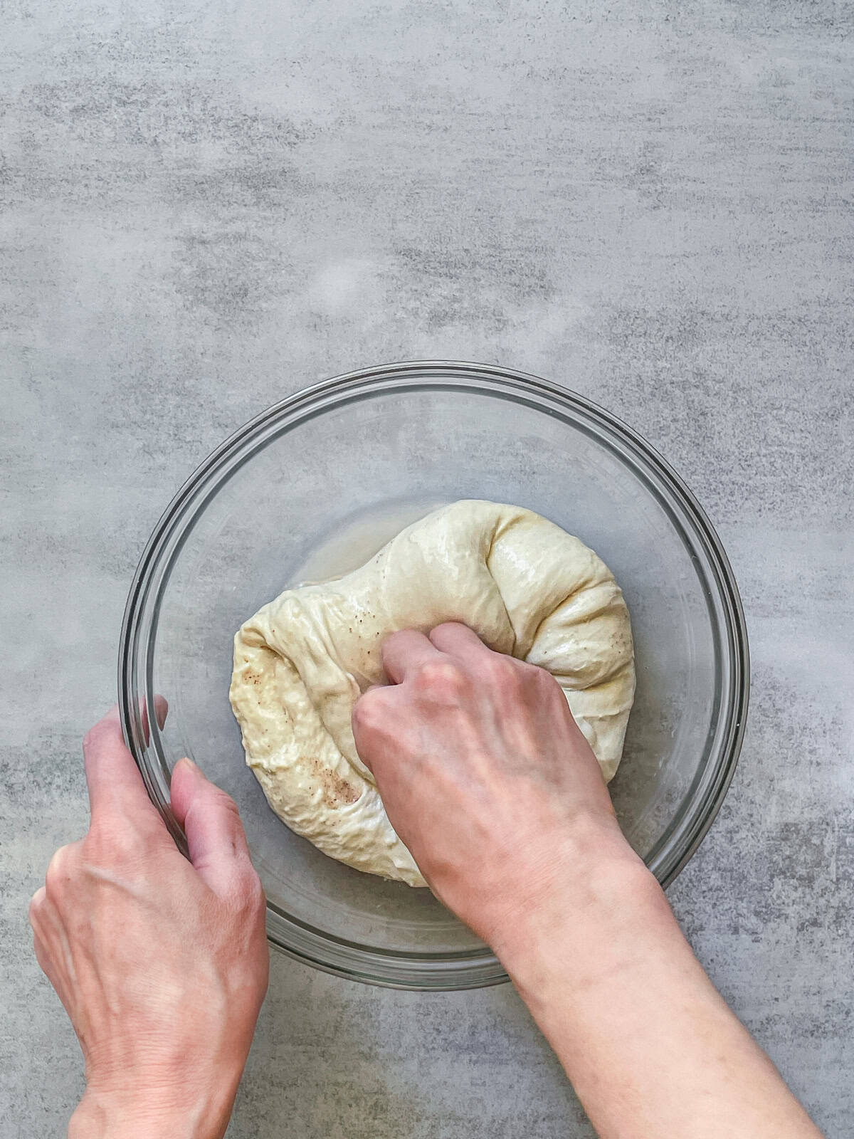 A hand folding bread dough toward the center in a bowl.
