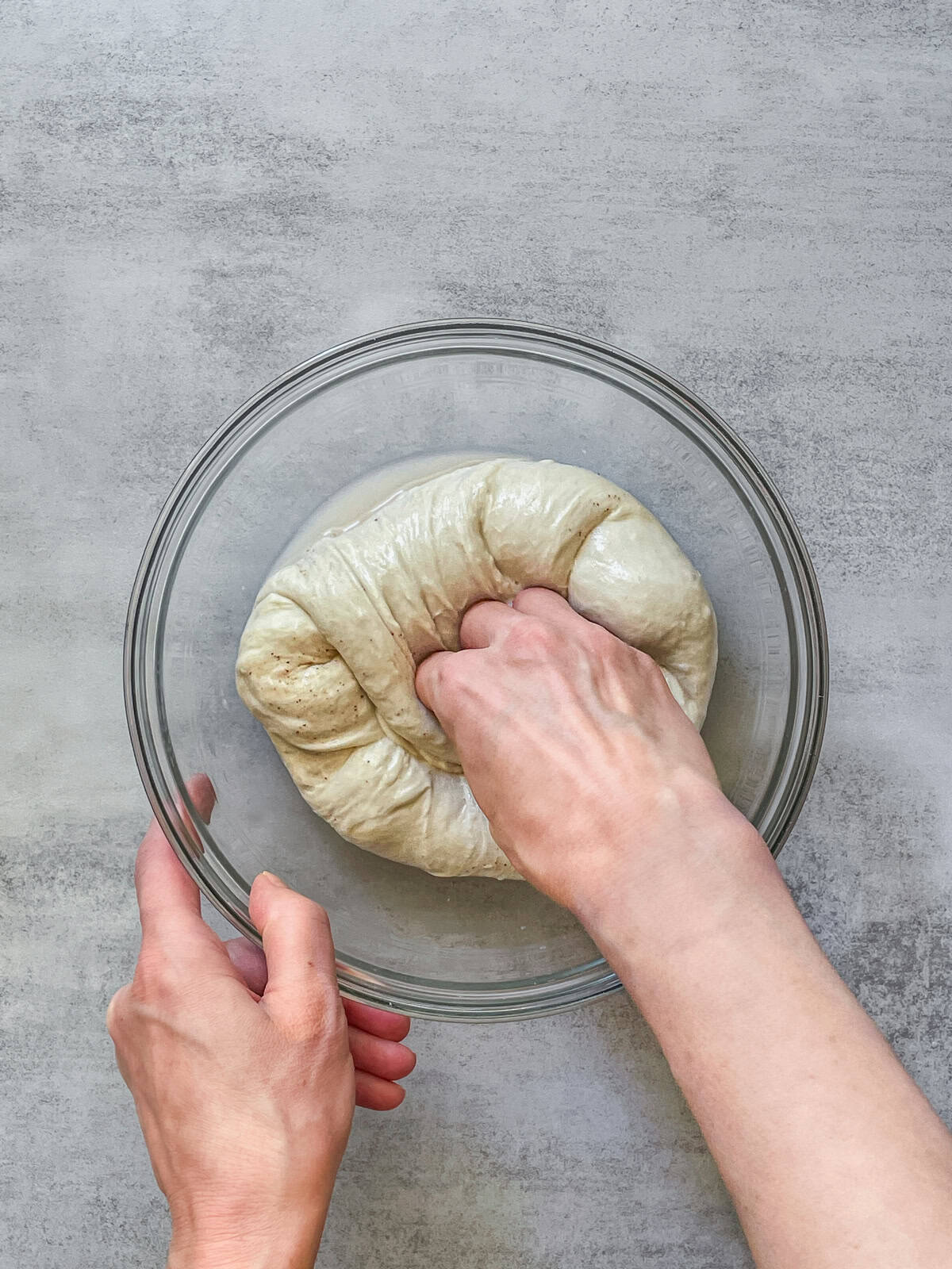 A fist pressing into the center of bread dough in a bowl.
