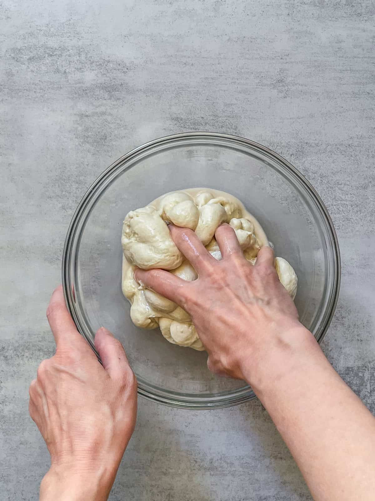 A hand squeezing bread dough in a bowl.