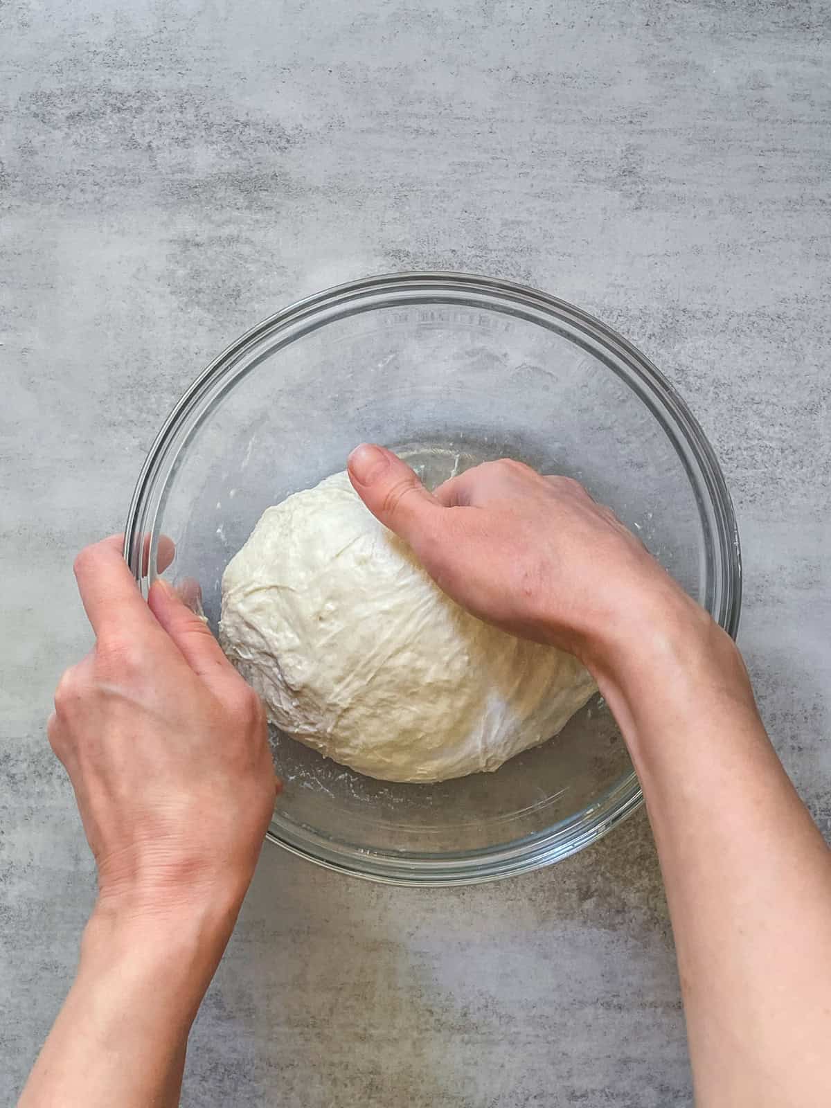 A hand grabbing bread dough in a glass bowl.