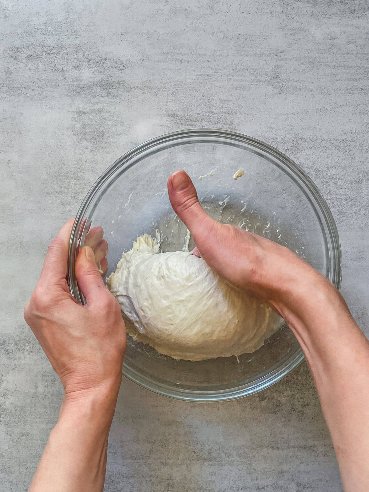 A hand grabbing bread dough in a glass mixing bowl.