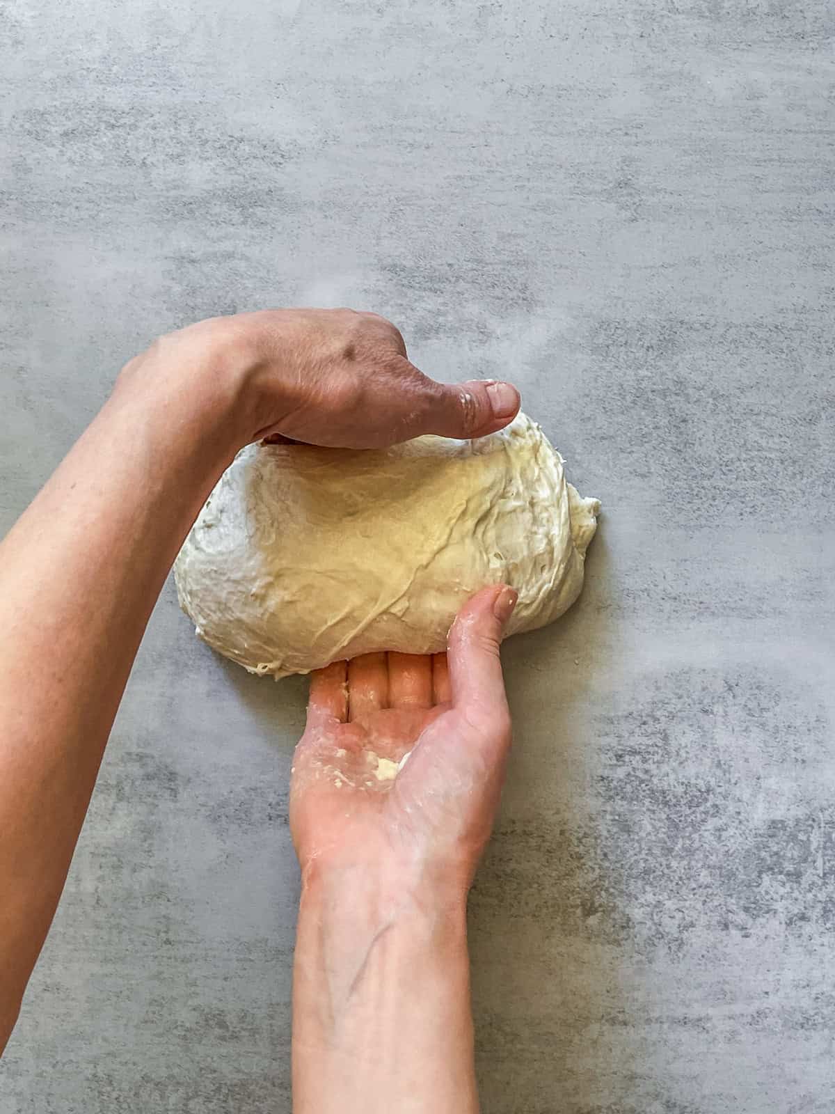 Both hands rotating bread dough on a table.