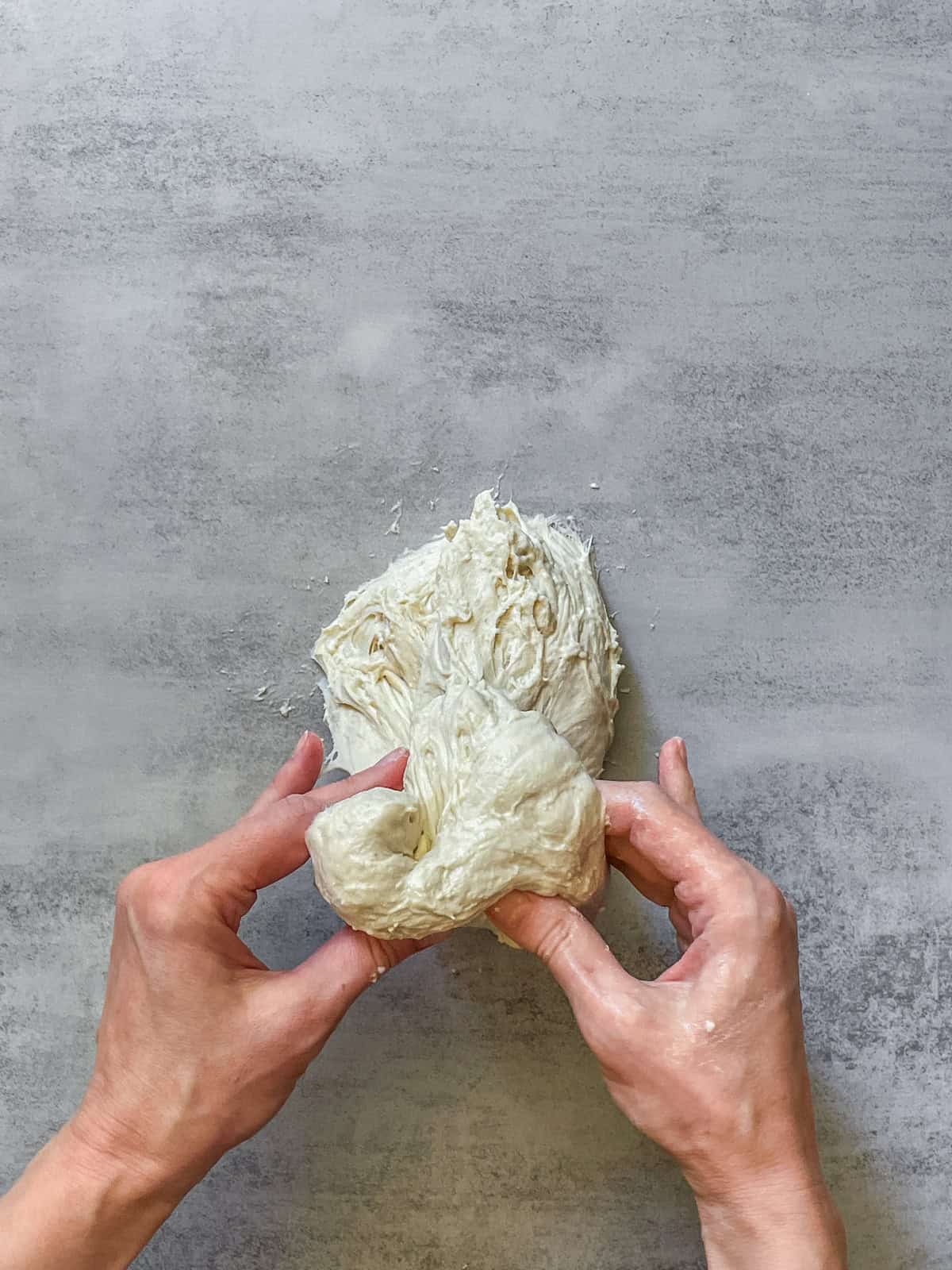 Both hands pulling bread dough on a table.