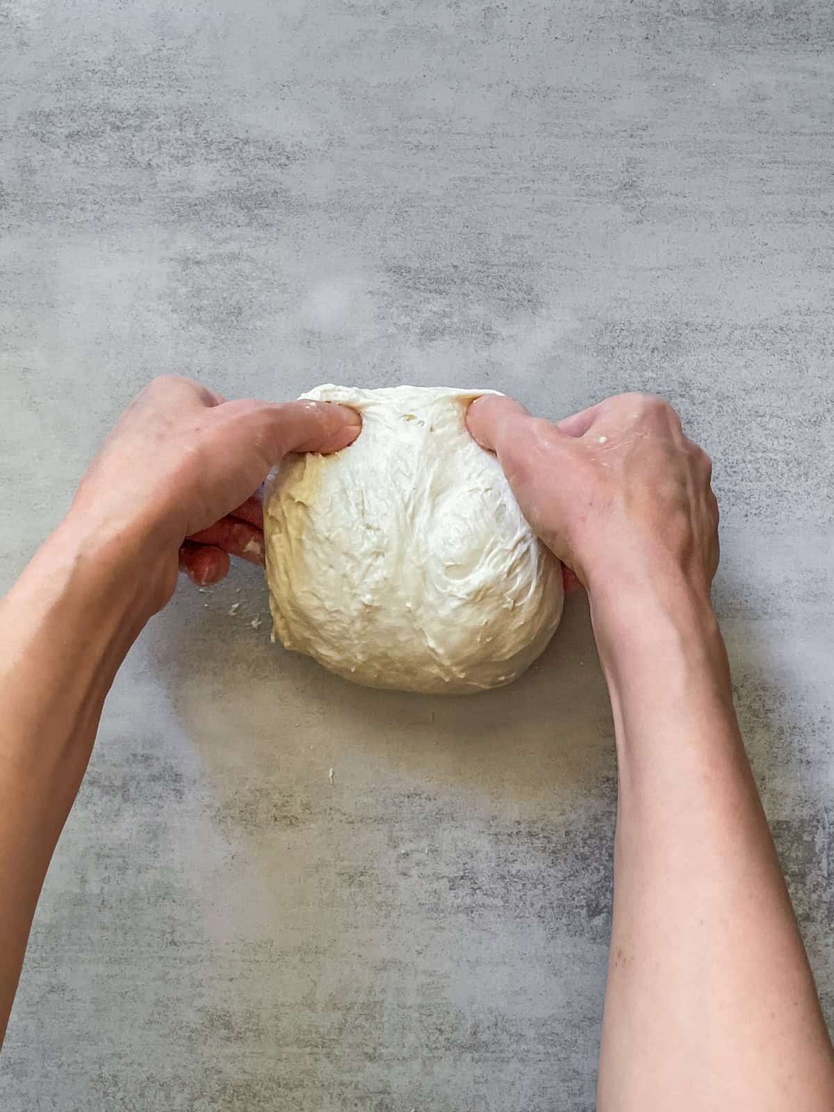 Hands folding bread dough on a table.
