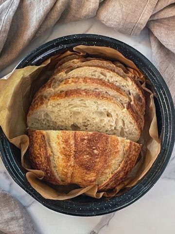 Sliced sourdough loaf resting in a roasting pan with a towel.