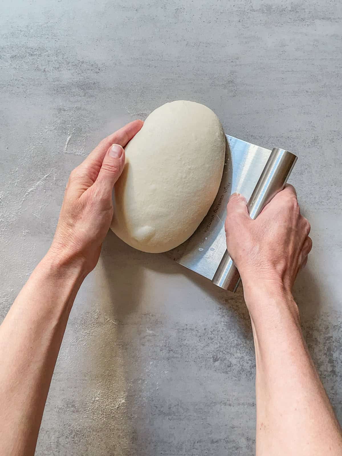Hands turning a ball of bread dough.