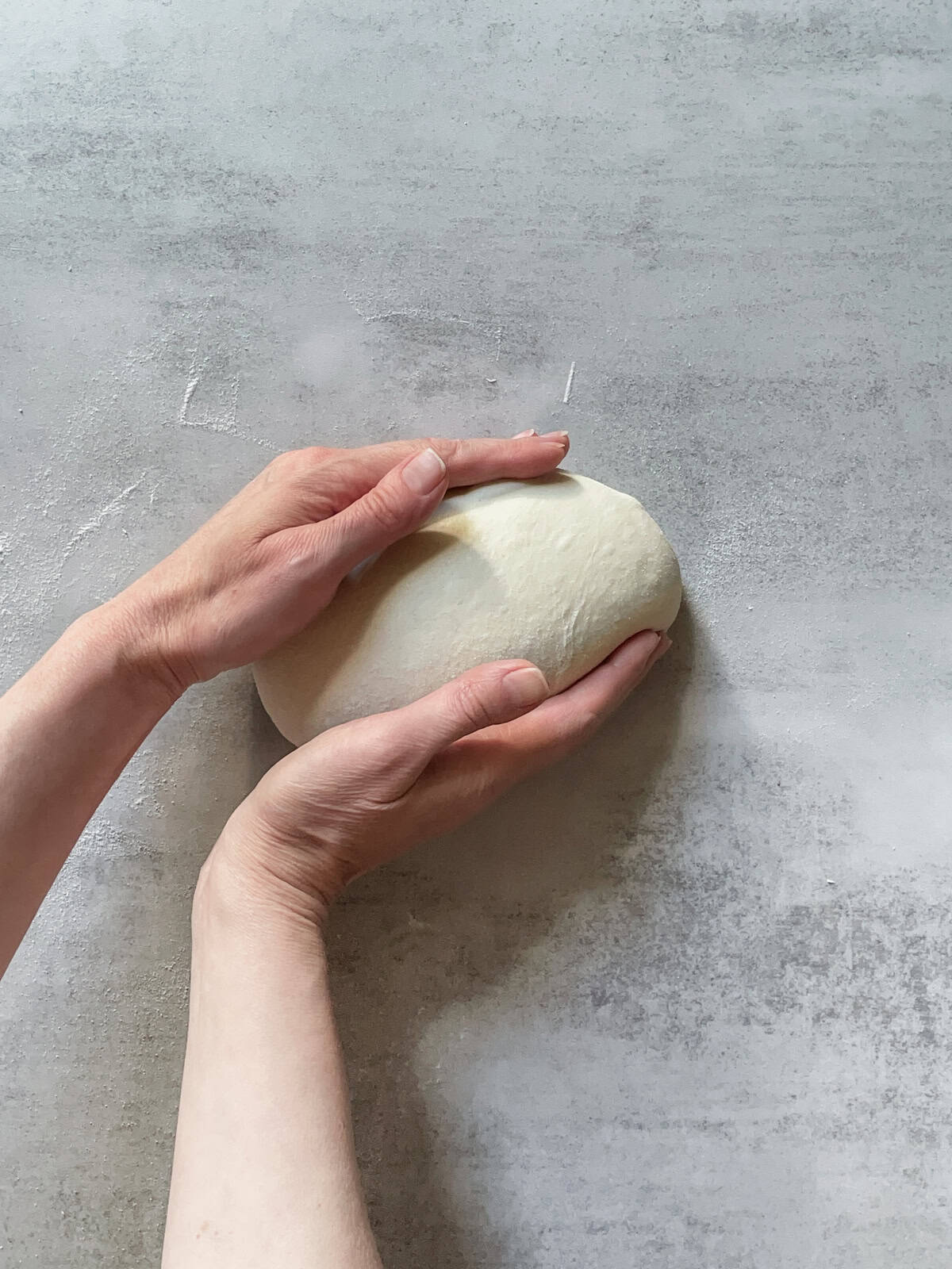 Hands holding a ball of bread dough.